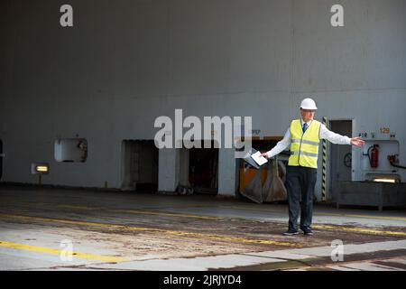 Logistics worker, manager or engineer, working in a shipping yard or cargo dock. Port employee, giving direction to load container for safety, storage Stock Photo