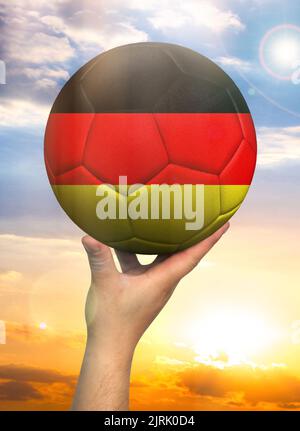 Soccer ball in hand with a depiction of the flag of Germany against a colorful sky Stock Photo