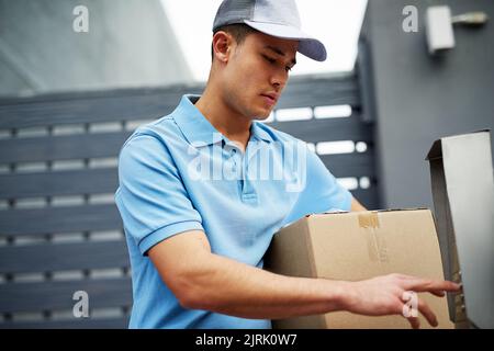 Doing his delivery rounds. a courier ringing an intercom while making a delivery. Stock Photo