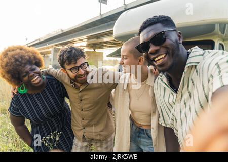 Interracial friendship. Group of happy close friends, reunited on their camping van trip, traveling through the country. Laughing and taking selfies together near the river. High quality photo Stock Photo
