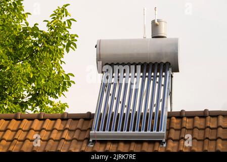 stainless steel thermal solar panel heater boiler  heating water roof of a house green tree vacuum air collectors clay roof tiles Stock Photo