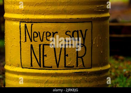 metal barrel painted yellow never say never wordd concept message card motivational quote text Stock Photo