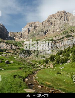 Green grassy valley with winding trails between mountain slopes located against rough rocky cliffs in nature of Spain in Pyrenees Stock Photo