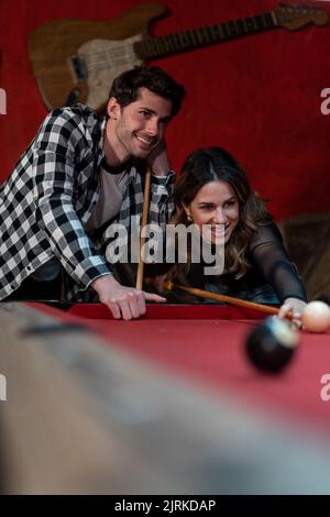 Cheerful couple with cues playing pool game in pub while enjoying weekend together Stock Photo