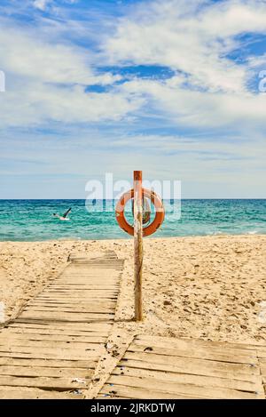 Lifebuoy on wooden post on sandy coast with footpath against flying seagull over endless ocean in sunlight in Fuerteventura Spain Stock Photo