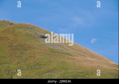 Green grassy Escuain valley located against clear blue sky with white moon on sunny summer day in nature of Spain Stock Photo