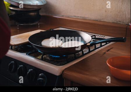 Pan with Venezuelan arepas frying on rack of gas stove in kitchen at home Stock Photo