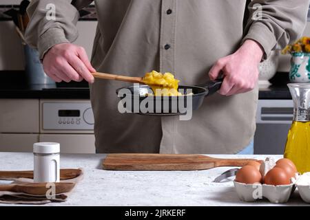 Unrecognizable crop male chef with delicious cooked Spanish omelette in frying pan standing at table in kitchen at home Stock Photo
