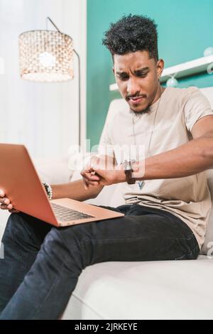 Frown African American male freelancer looking at time while working on netbook at home Stock Photo