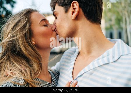 Happy couple in trendy clothes standing in city street and kissing each other with love Stock Photo