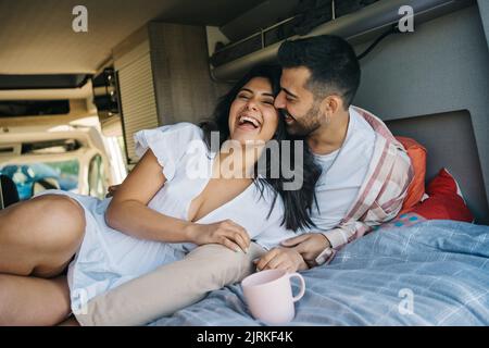 Tender Hispanic traveling couple laughing together on bed and cuddling in caravan while enjoying trip Stock Photo