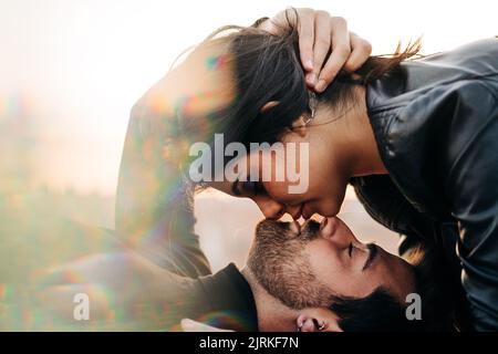 Side view of bearded ethnic man embracing head of girlfriend in leather jacket while kissing in daytime Stock Photo