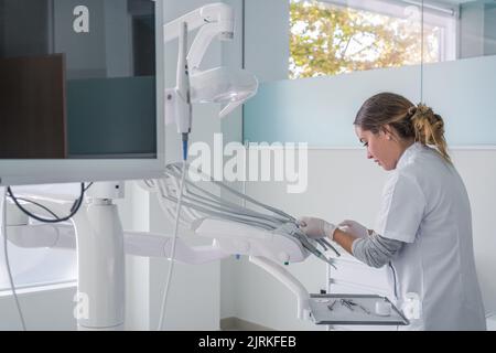 Side view of woman in medical uniform adjusting tools settings while standing in light dental office before curing procedure Stock Photo