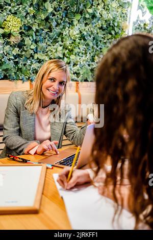 Adult content business trainer with laptop near crop anonymous female employee taking notes during coaching process Stock Photo