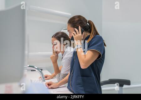 Side view of medical practitioners browsing data on modern computer while working in lab of modern hospital together and speaking on the mobile phone Stock Photo