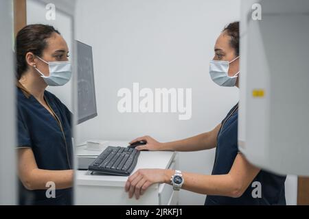 Side view of woman in medical uniform looking at teeth X ray on computer monitor while working in lab of contemporary dental clinic Stock Photo