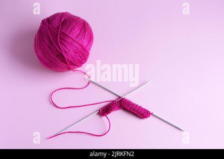 Pink knitted wool on a pink background with knitting needles, hobby Stock Photo