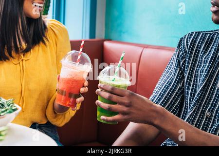 Smiling multiracial partners with healthy drinks talking while looking at each other against tables with assorted tasty food Stock Photo
