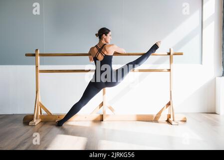 Young woman dancer doing a stretching routine on a wooden barre at dance studio Stock Photo