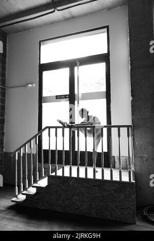 Black and white photo of young woman dancer doing a stretching routine at the entrance of dance studio Stock Photo