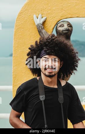 Smiling ethnic male in black t shirt with Afro hairstyle looking at camera against animal sculpture outdoors Stock Photo