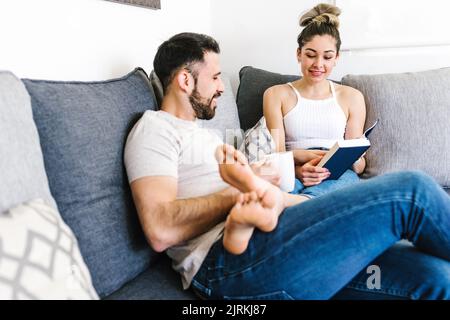 Content ethnic couple sitting on sofa together relaxing at weekend at home Stock Photo