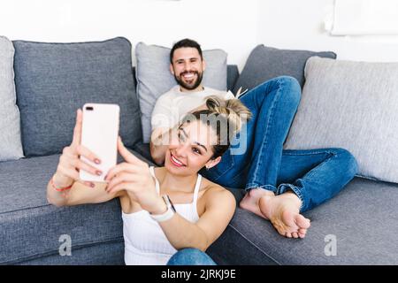 Positive ethnic couple sitting in living room at home and taking self shot on mobile phone Stock Photo