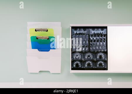 Assorted clipboards in folder rack near X ray image of teeth on wall in hospital Stock Photo