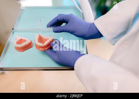 From above of crop unrecognizable orthodontist in sterile gloves with jaw casts and transparent braces in clinic Stock Photo