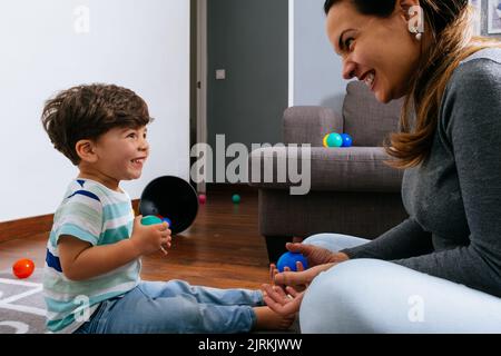 Adult woman and little boy sitting on hopscotch mat and arranging colorful balls in heap while playing in nursery together Stock Photo