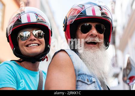 Crop of a happy modern senior couple with helmets and sunglasses riding on a motorcycle while driving through town Stock Photo