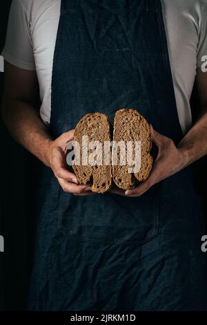 Crop unrecognizable male baker in apron demonstrating slices whole wheat bread in kitchen Stock Photo