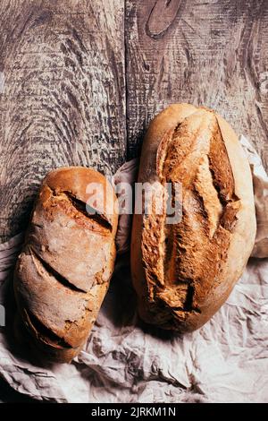 Top view of freshly baked delicious sourdough breads of various shapes placed on wooden table in bakery Stock Photo