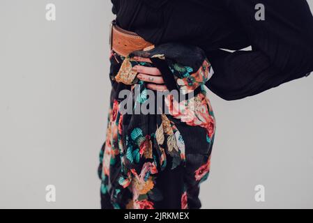 Side view of crop trendy slim female in black knitted sweater and colorful skirt in composition with brown leather belt standing with hand on hip agai Stock Photo