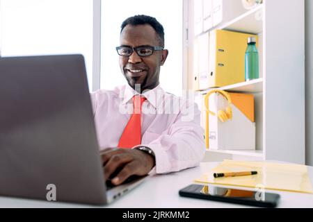 Smiling black male entrepreneur working on netbook in modern office Stock Photo