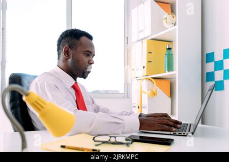 Side view of focused black male entrepreneur working on netbook in modern office Stock Photo