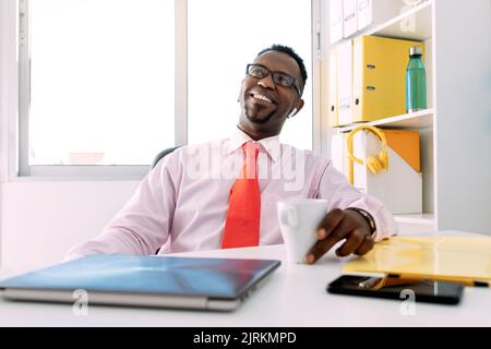 Smiling middle aged ethnic male executive in white shirt with tie and eyeglasses looking up in workspace Stock Photo