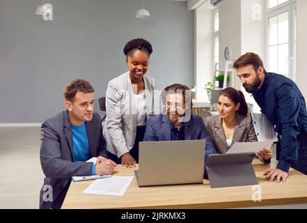 Diverse team of happy people use a laptop and tablet while working on a business project together Stock Photo