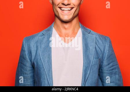 Unrecognizable young cool male in trendy wear and toothy smile on red background Stock Photo