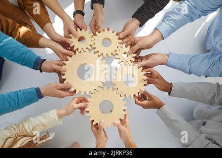 Business people or office workers hold wooden gears that symbolize well-coordinated teamwork. Stock Photo