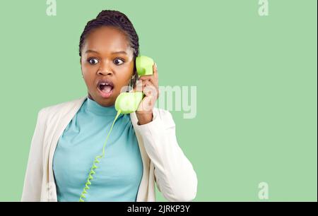 Amazed dark skinned young woman talking on landline phone isolated on light green background. Stock Photo
