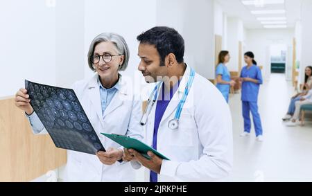 Two doctors analyzing MRI scan of patient's brain and diagnosing illness while standing in corridor of modern clinic during working day. medical teamw Stock Photo