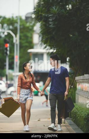 Happy couple with shopping bags holding hands when walking outdoors Stock Photo