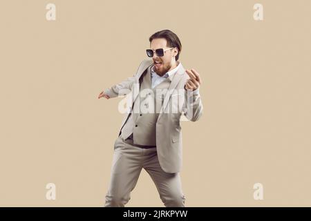 Cheerful cool man in three-piece suit rejoices and has fun dancing on beige background. Stock Photo