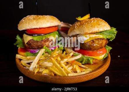 Two homemade beef burgers with mushrooms, micro greens, red onion, fried eggs and beet sauce on wooden cutting board. Side view, close up Stock Photo