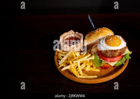 Close-up of beef burger with fried egg on black background. Hamburger - bun, grilled meat burger, lettuce, tomato and fried egg. Stock Photo