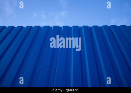 Texture of a metal blue painted old dark fence wall with a sky in the background. Stock Photo