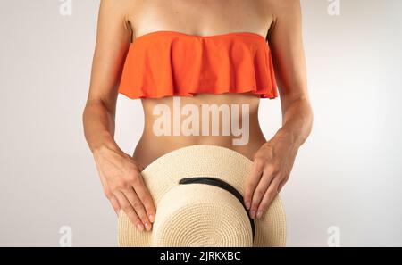 Slender female body in an orange swimsuit top, the bottom covers with a straw hat - summer. High quality photo Stock Photo