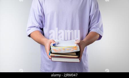 Male student holds a stack of notebooks and books on a white background. Stock Photo