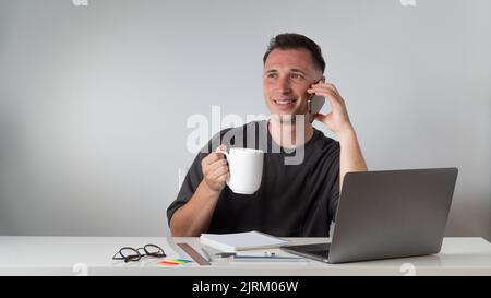 A student at a laptop talks on the phone and drinks coffee - a break for rest Stock Photo
